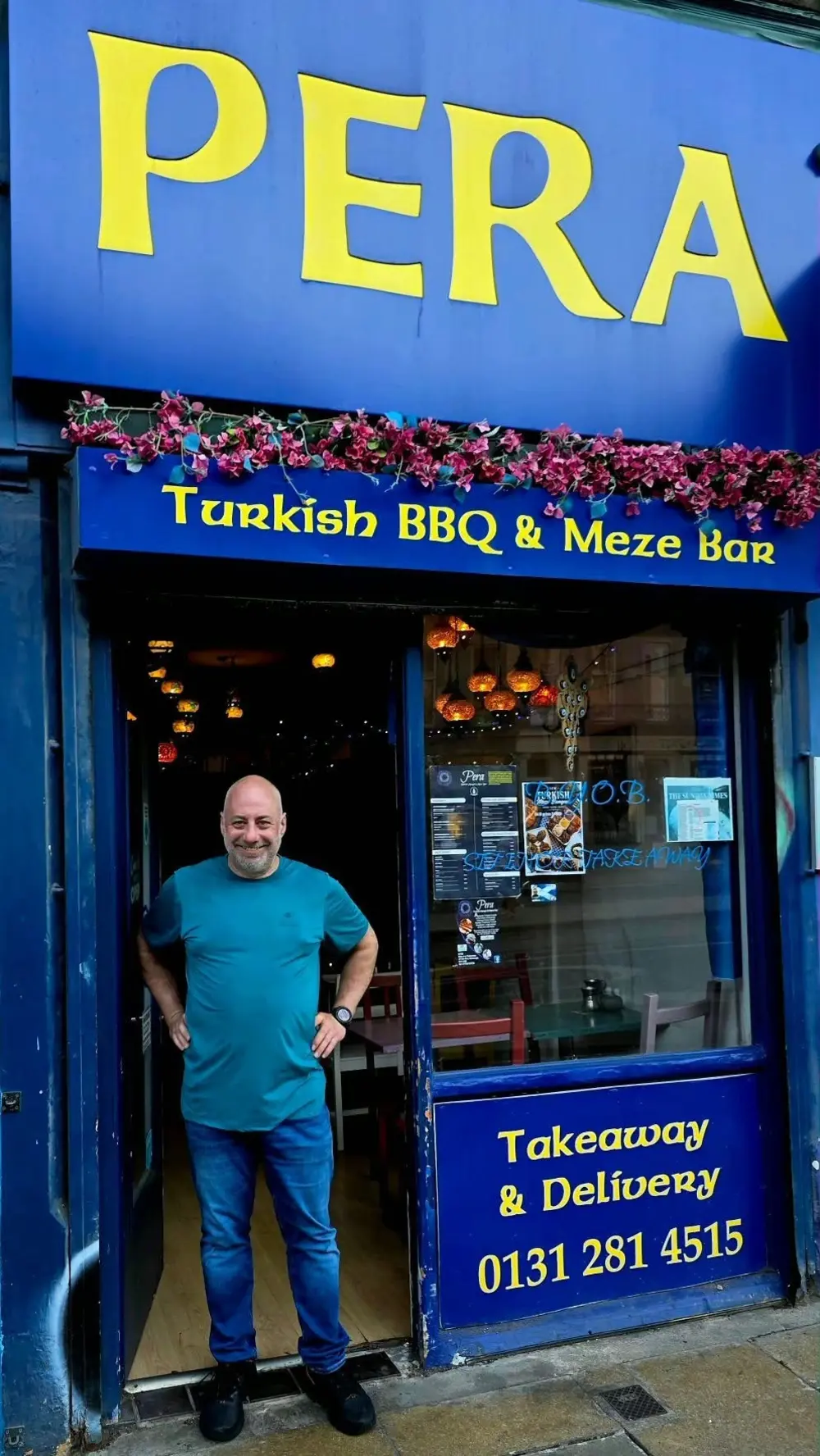 Pera's blue and yellow shopfront on Elm Row, with the owner at the door